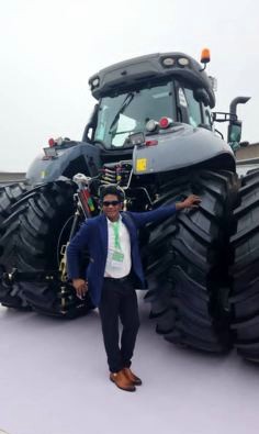 KCCIMA delegate standing between the rear wheels of a large grey tractor